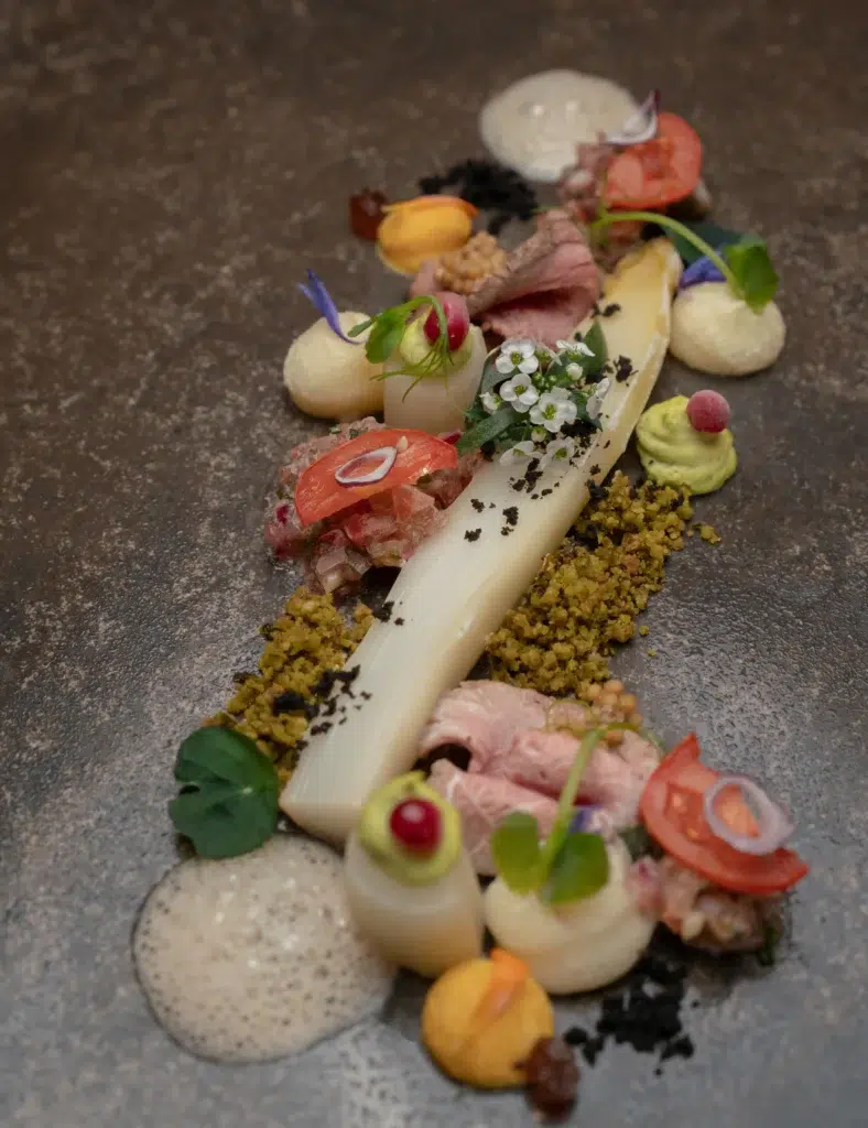 Elegantes Restaurantgericht mit weißem Spargel, bunten Garnituren, Schaum und essbaren Blüten.