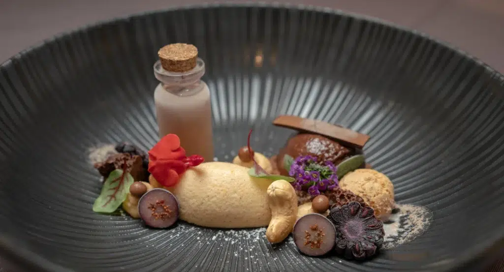 Ein Gourmet-Dessert im Restaurant-Stil mit Mousse, Schokolade, Früchten und einer verschlossenen Flasche.