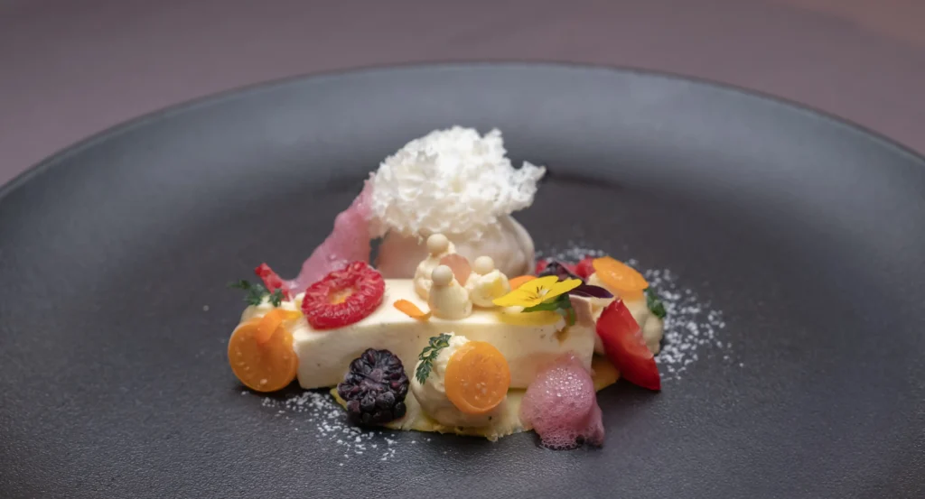 Gourmet-Dessert auf einem Vista Allegra-Teller mit Früchten, essbaren Blüten, Mousse und weißer Garnitur.