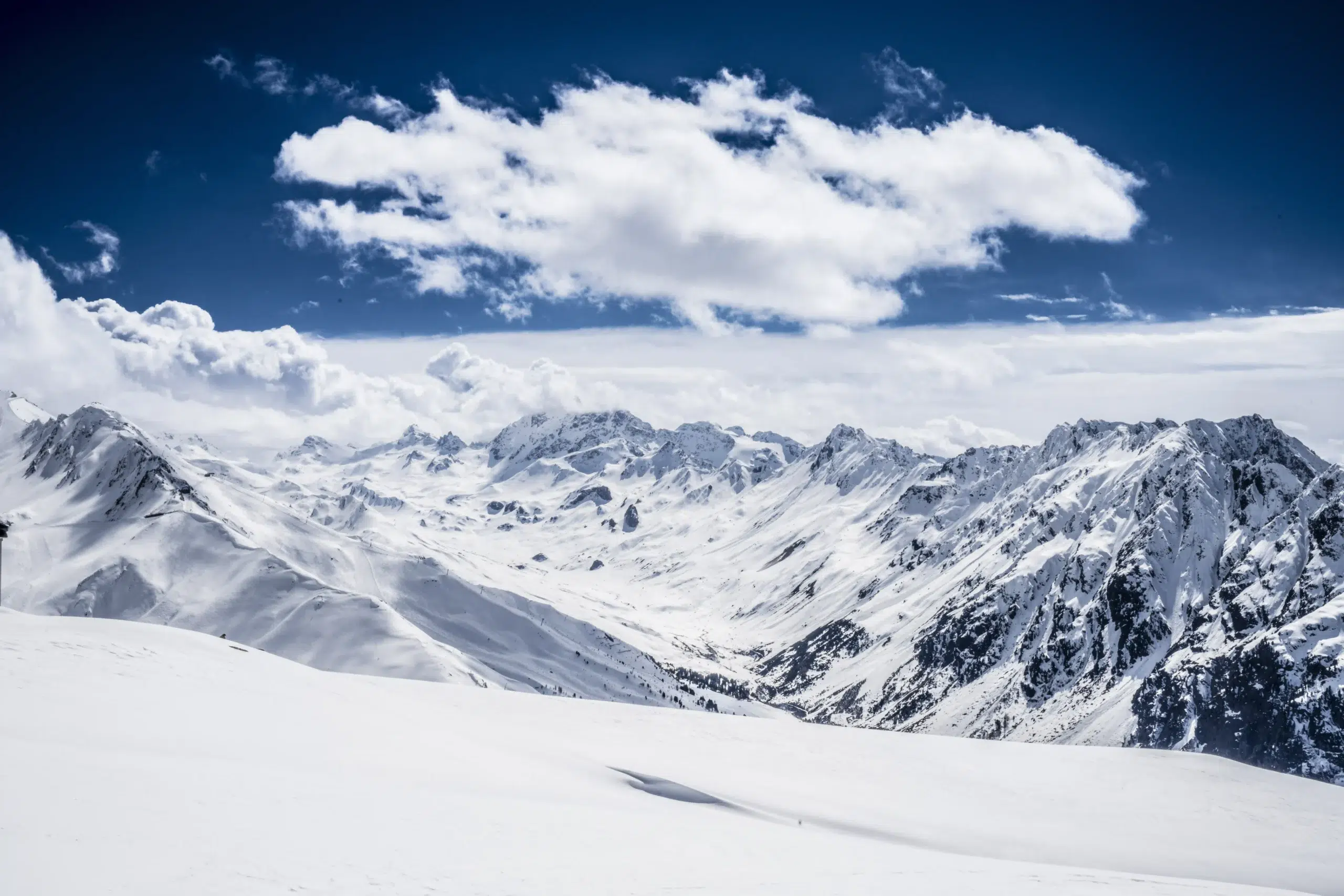 Schneebedeckte Berge fangen die heitere Schönheit des Winters unter einem blauen, wolkenverhangenen Himmel ein.