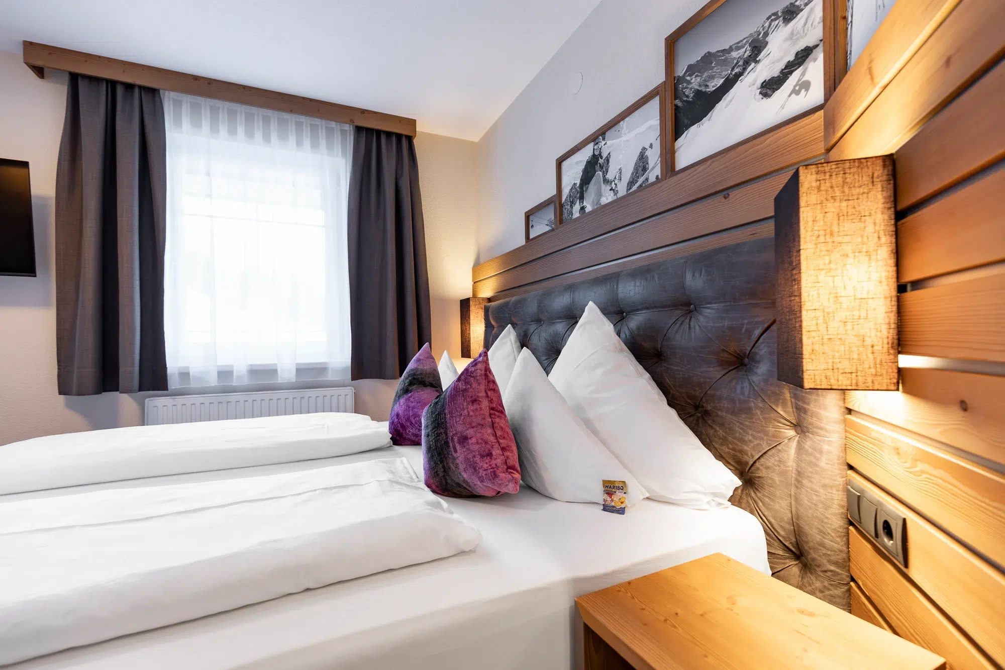 Modernes Zimmer mit ordentlich gemachtem Bett, lila Kissen und stilvollem Holzdekor.