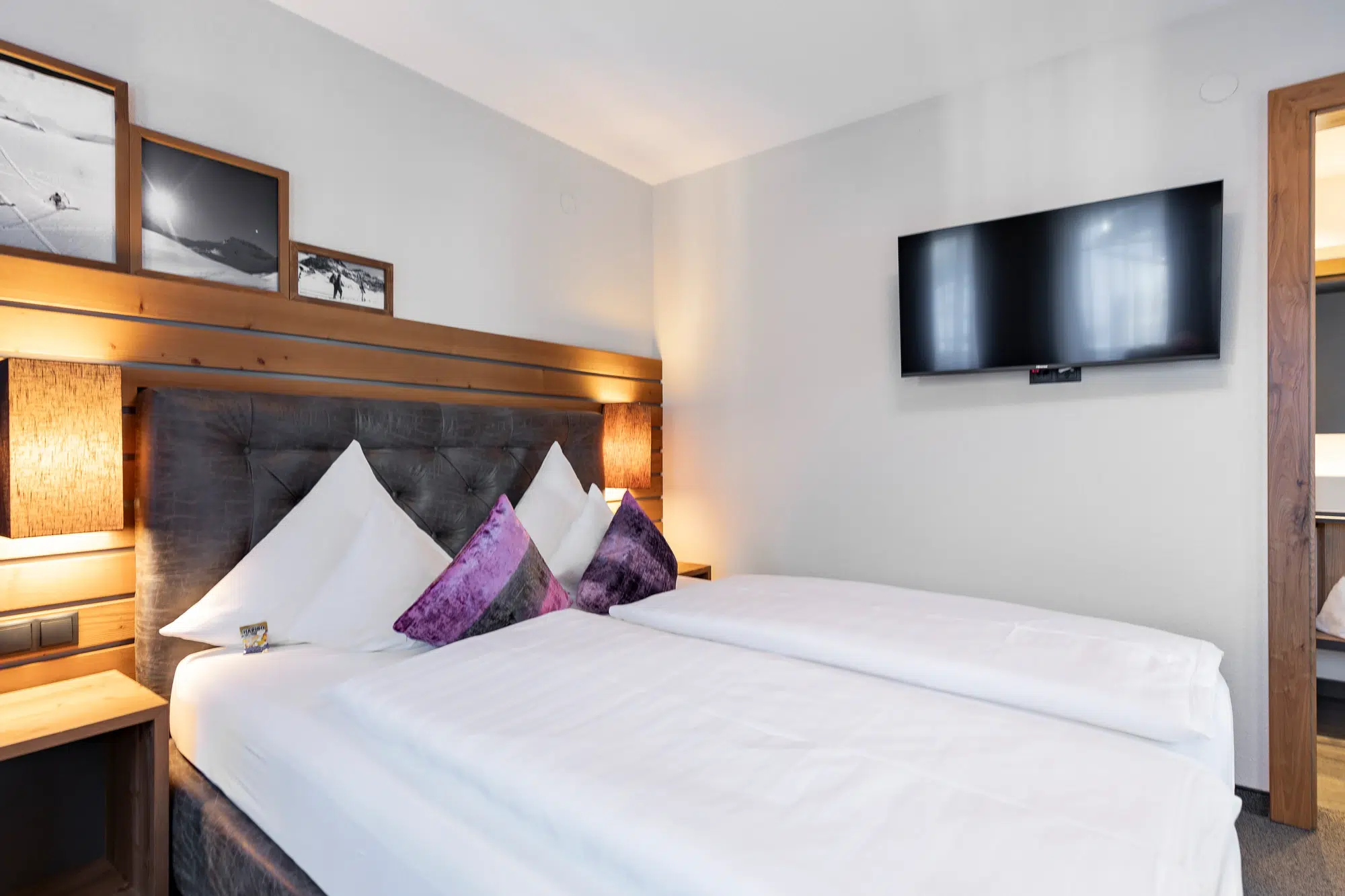 Modernes Zimmer mit Doppelbett, Wandfernseher und gemütlicher Beleuchtung.
