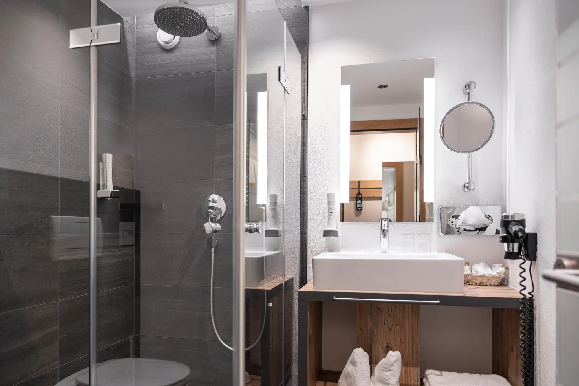 Modernes Zimmer-Badezimmer mit Glasdusche, weißem Waschbecken, Spiegel und Holzakzenten.