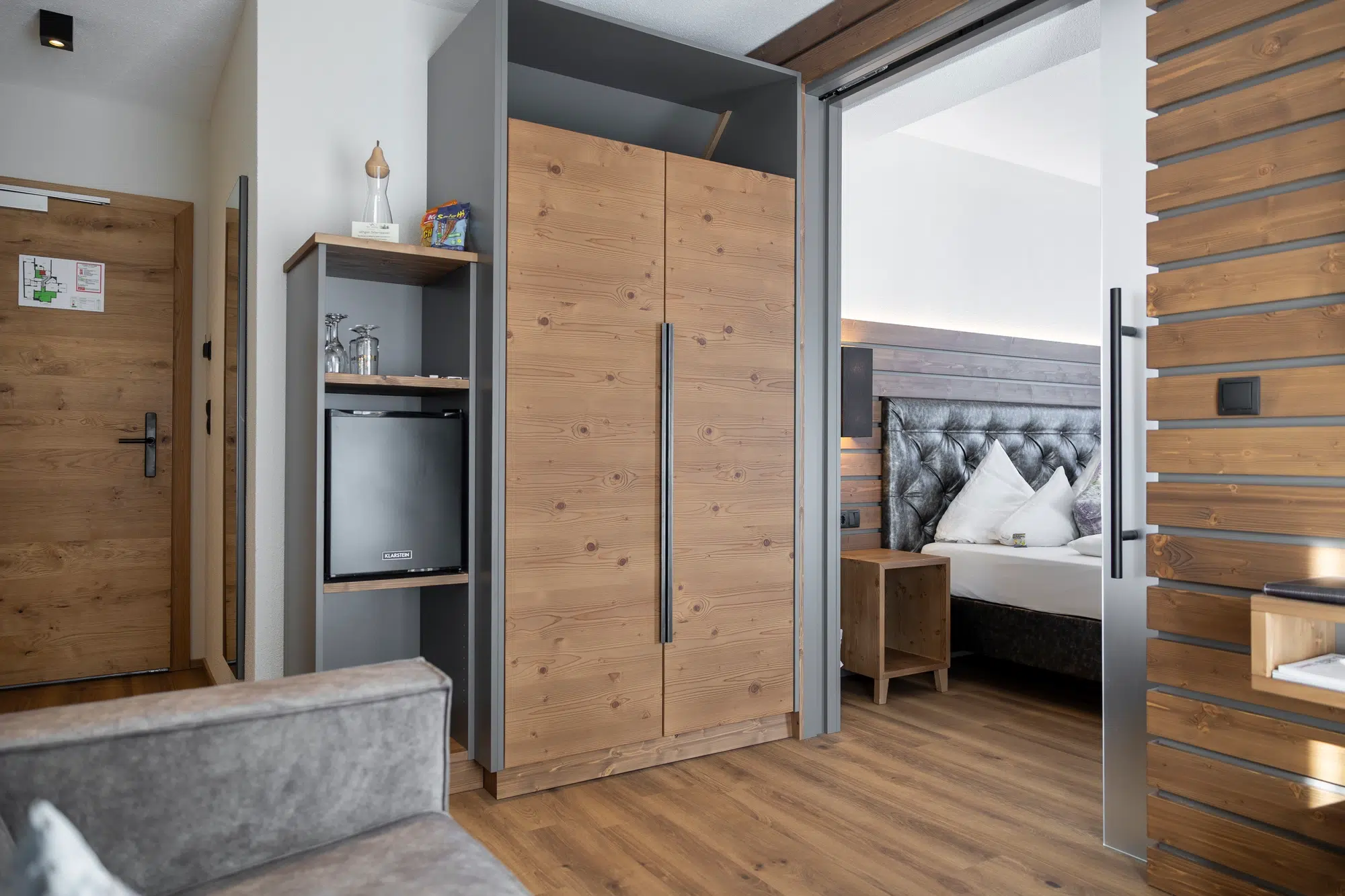 Modernes Zimmer mit Holzschrank, Minikühlschrank und Bett mit weißen Kissen im Hintergrund.