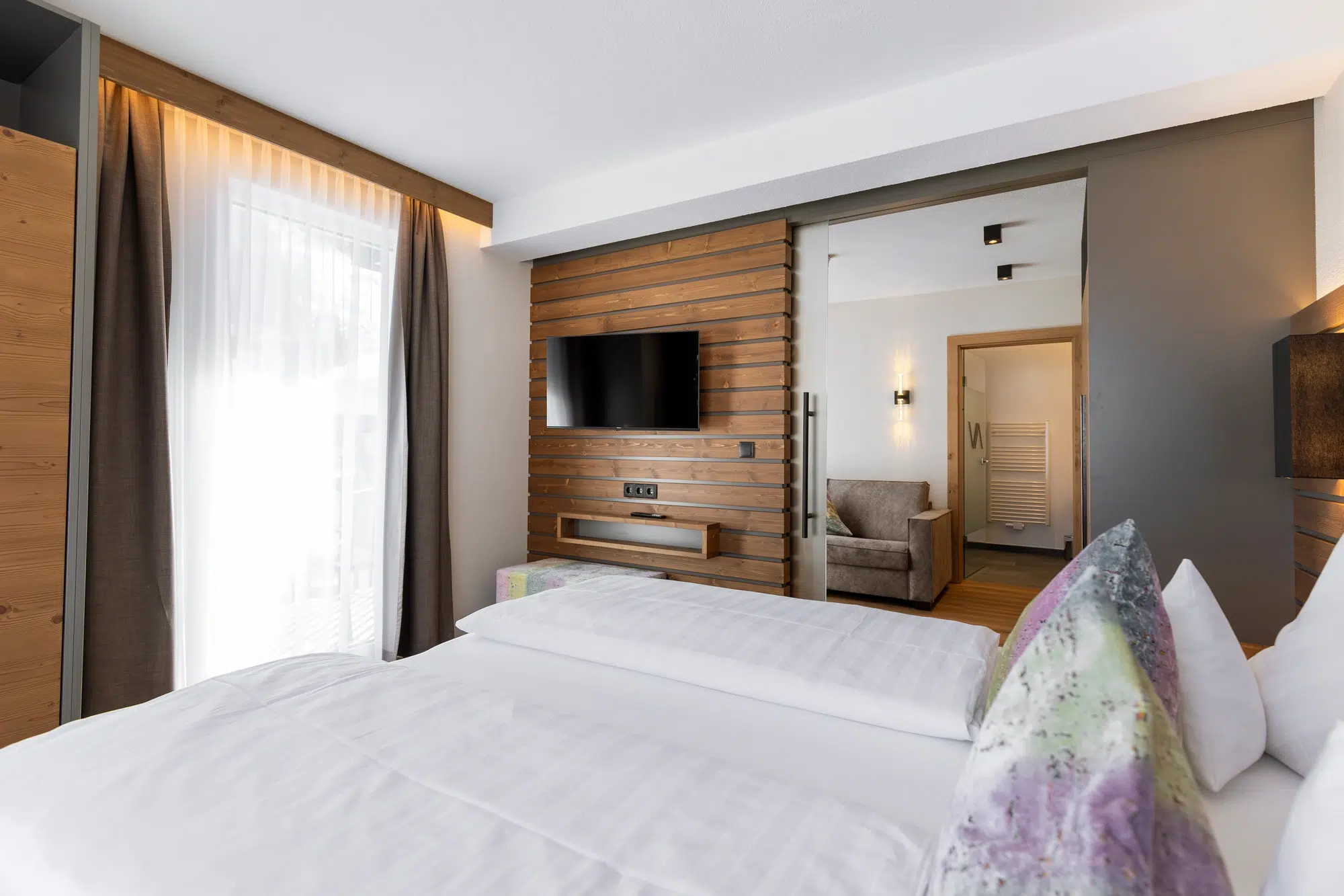 Modernes Zimmer mit Doppelbett, Fernseher und gemütlicher Sitzecke im Hintergrund.