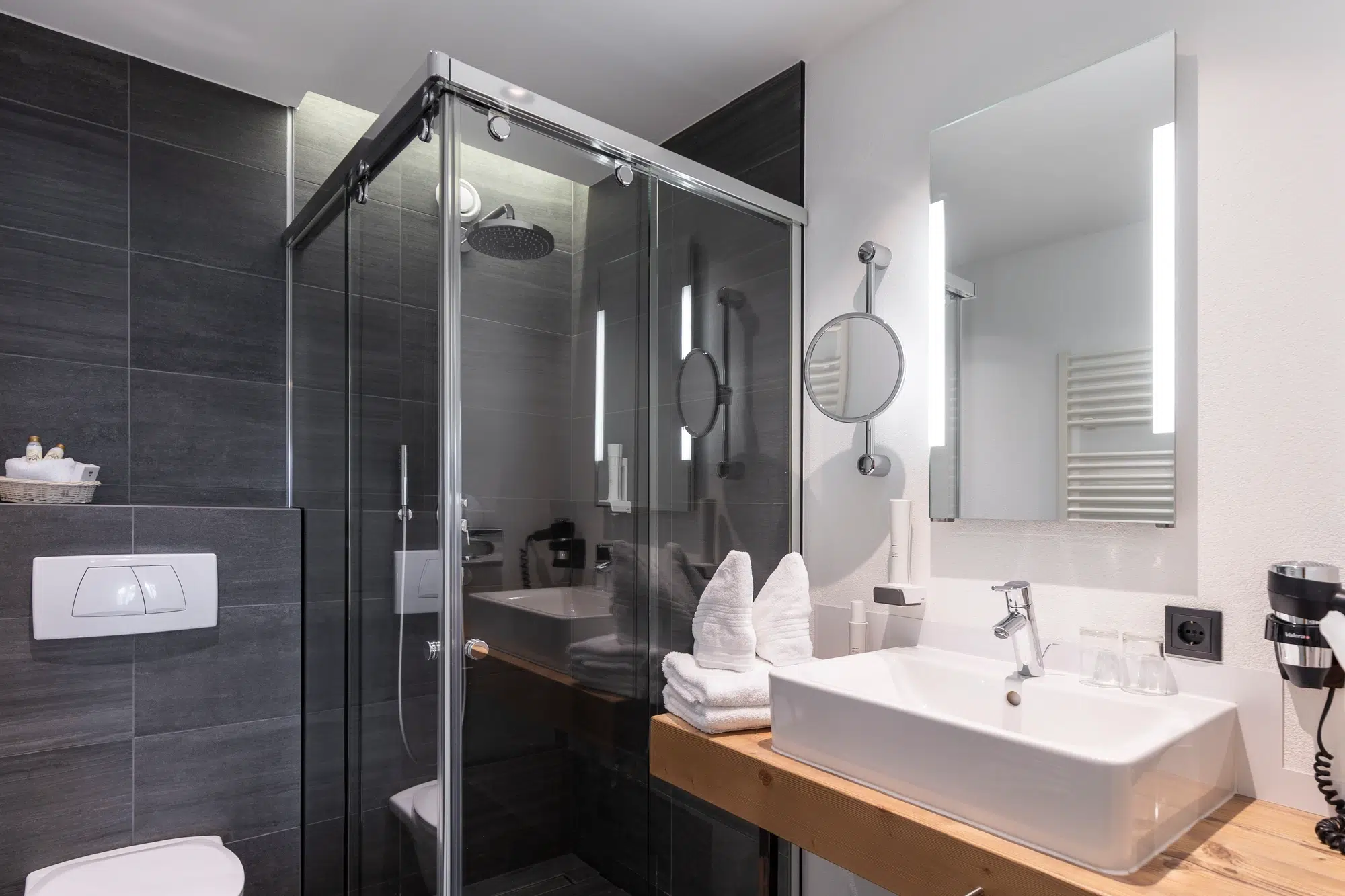 Modernes Zimmer-Badezimmer mit Glasdusche, weißem Waschbecken, frischen Handtüchern und Wandspiegel.