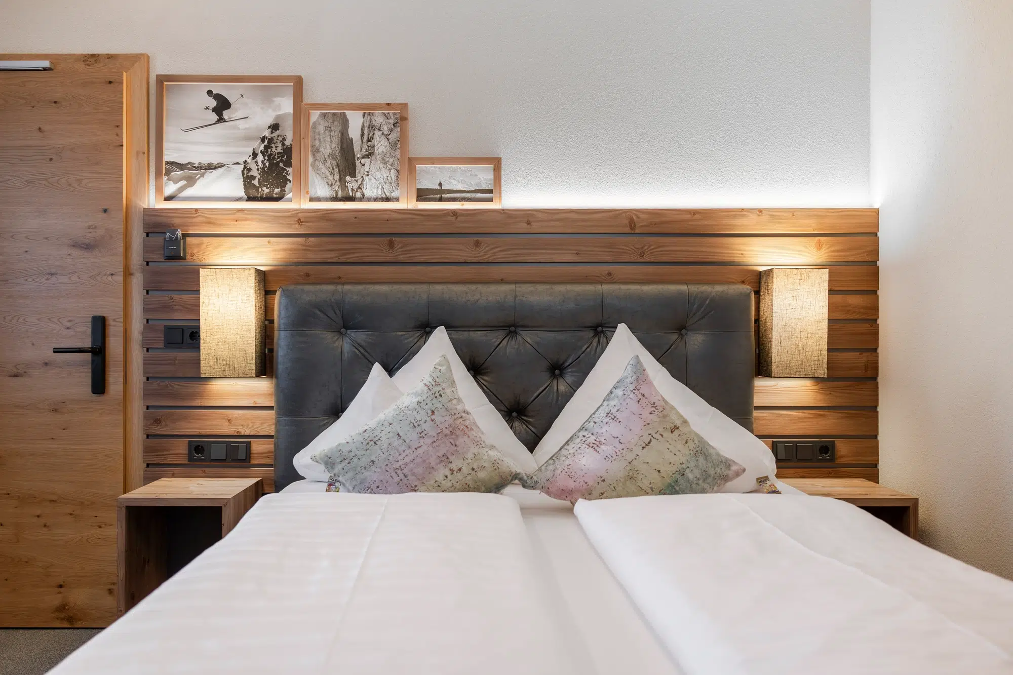 Modernes Zimmer mit Doppelbett, Holzakzenten und gerahmten Fotos über dem Kopfteil.
