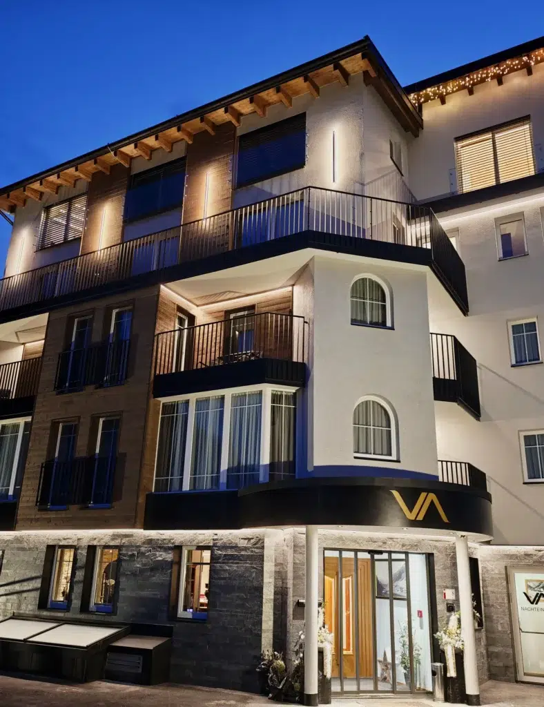 Modernes Vista Allegra Hotel mit Balkonen, nachts warm beleuchtet, von der Straße aus gesehen.