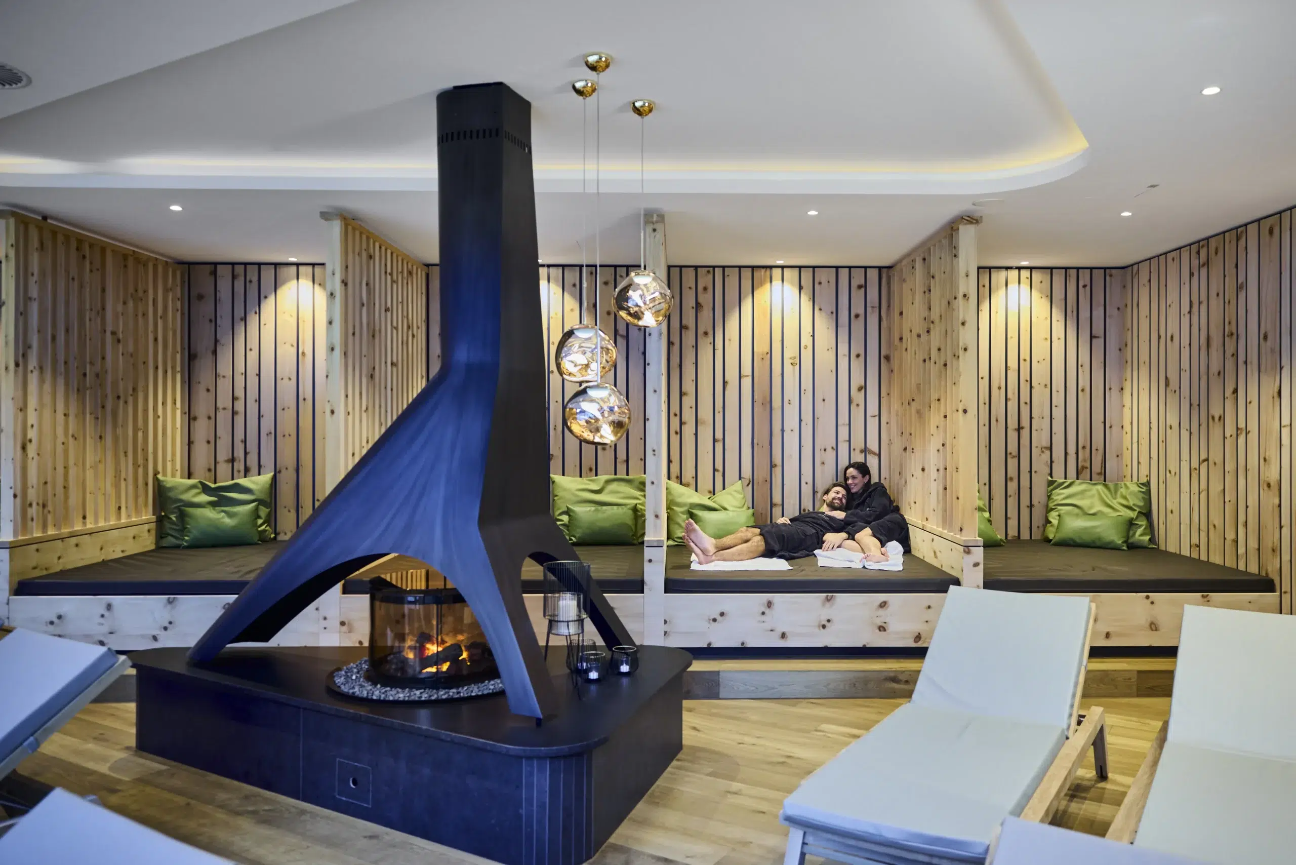 Moderne Lounge in einem Wellnesshotel mit Kamin, Holzwänden und grünen Kissen.