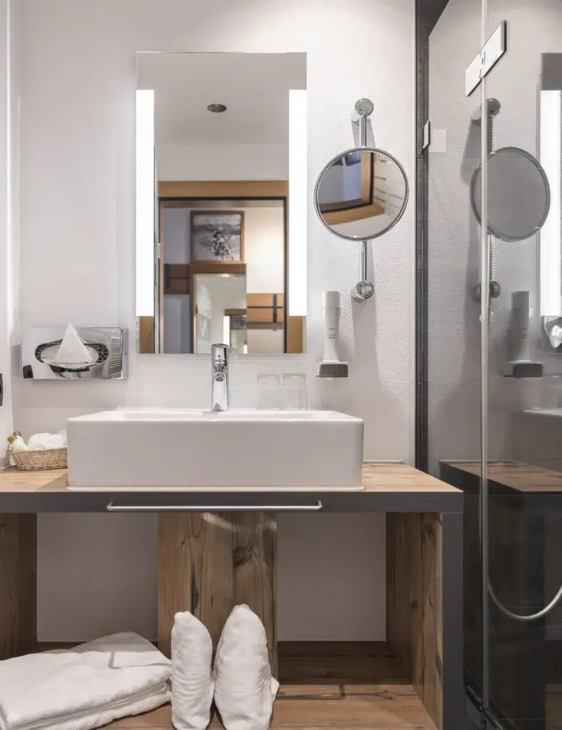Modernes Vista Allegra-Badezimmer mit quadratischem Waschbecken, rundem Spiegel, Handtüchern und Glasduschtür.