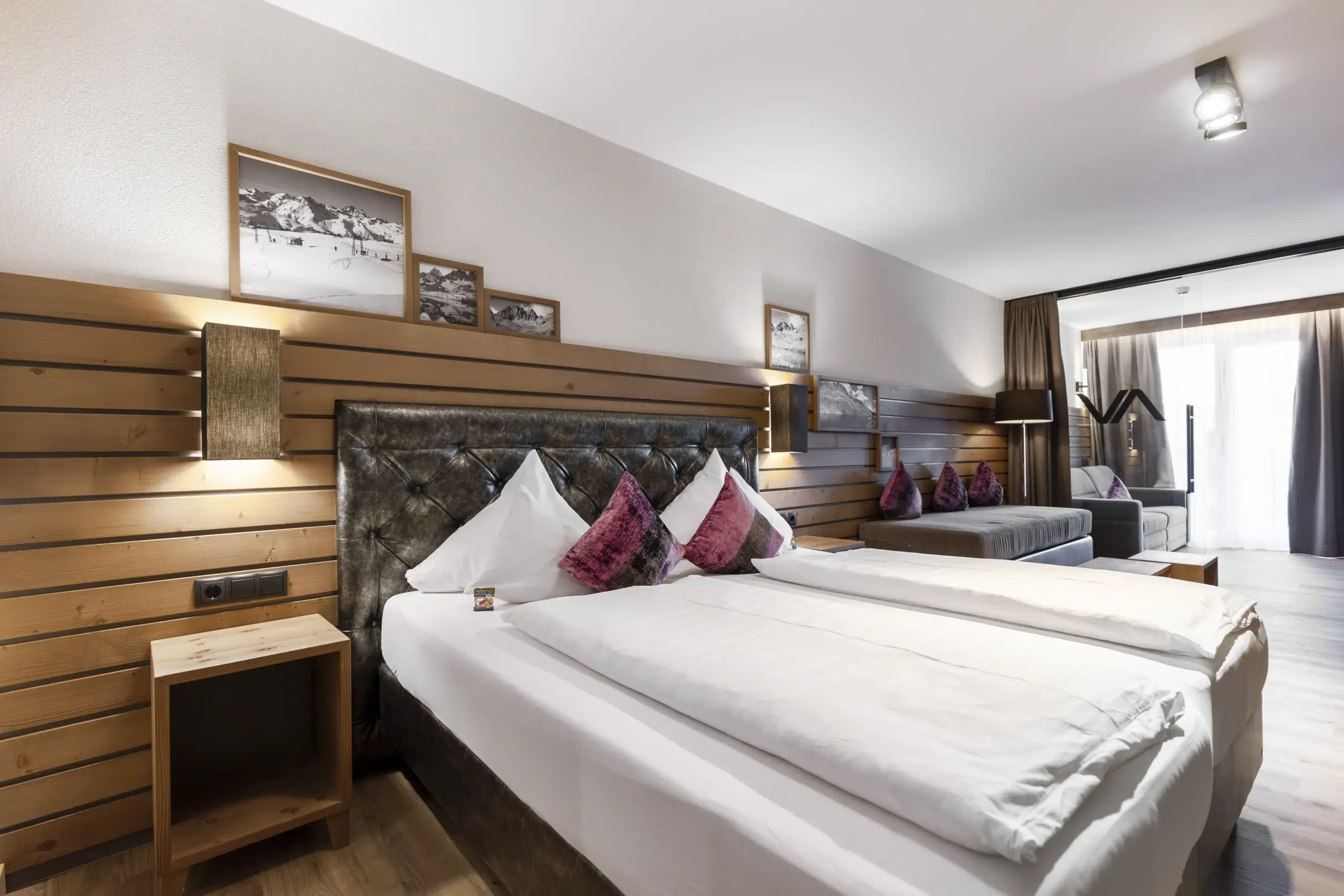 Modernes Hotelzimmer im Vista Allegra mit großem Bett, Sofa, Holzdekor und gerahmten Fotos.