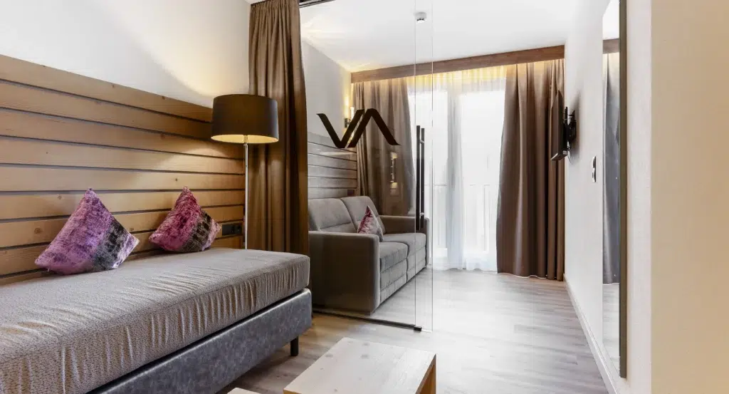 Modernes Vista Allegra-Hotelzimmer mit zwei Betten, Glastrennwand und warmen braunen Dekorakzenten.
