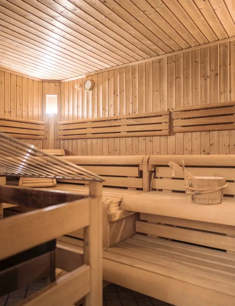 Holzsaunaraum mit Bänken, Eimer und Ofen in einem warm beleuchteten Wellnesshotel.