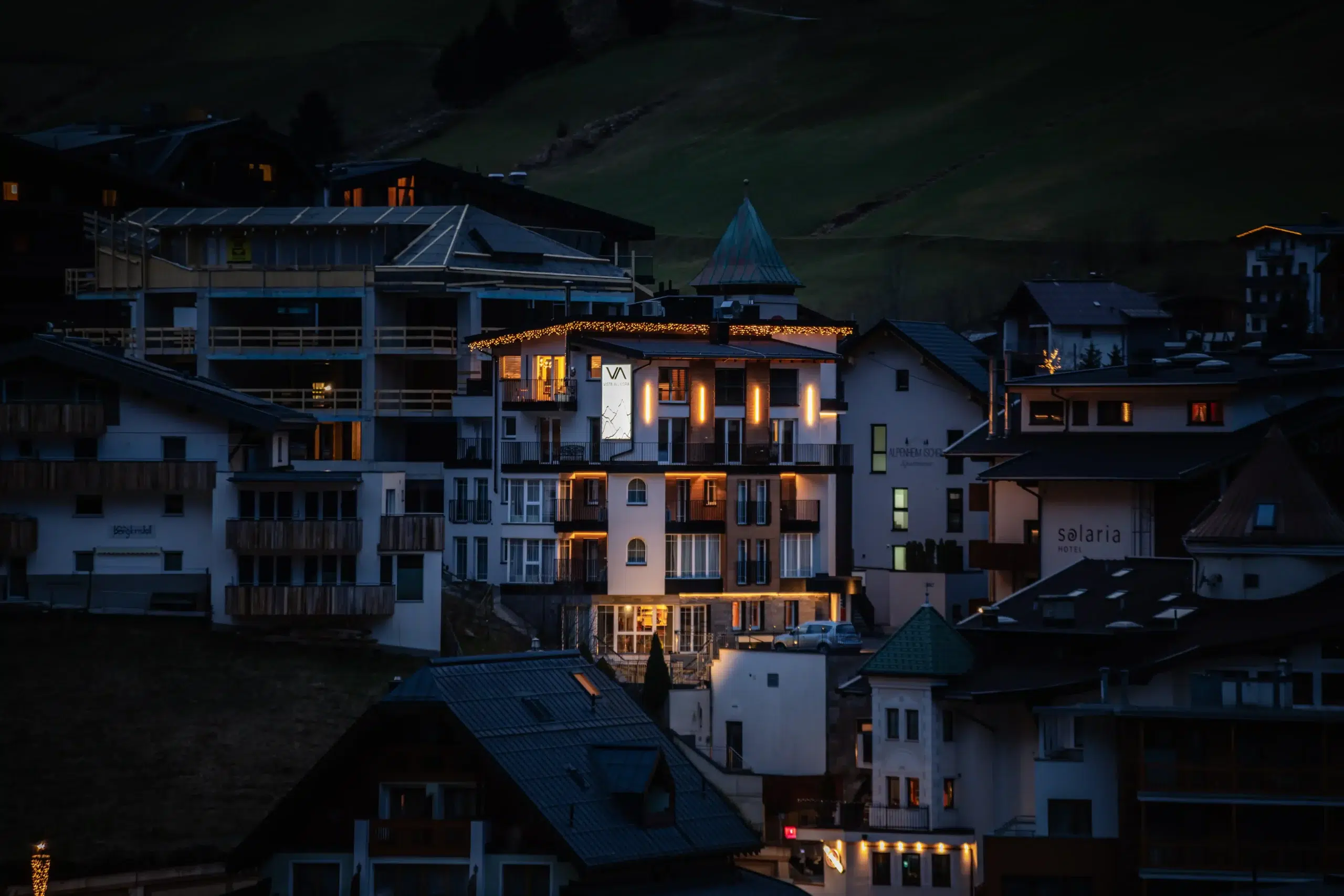 Eine Ansammlung warm beleuchteter Alpengebäude in der Abenddämmerung präsentiert die ideale Lage und Anreise.