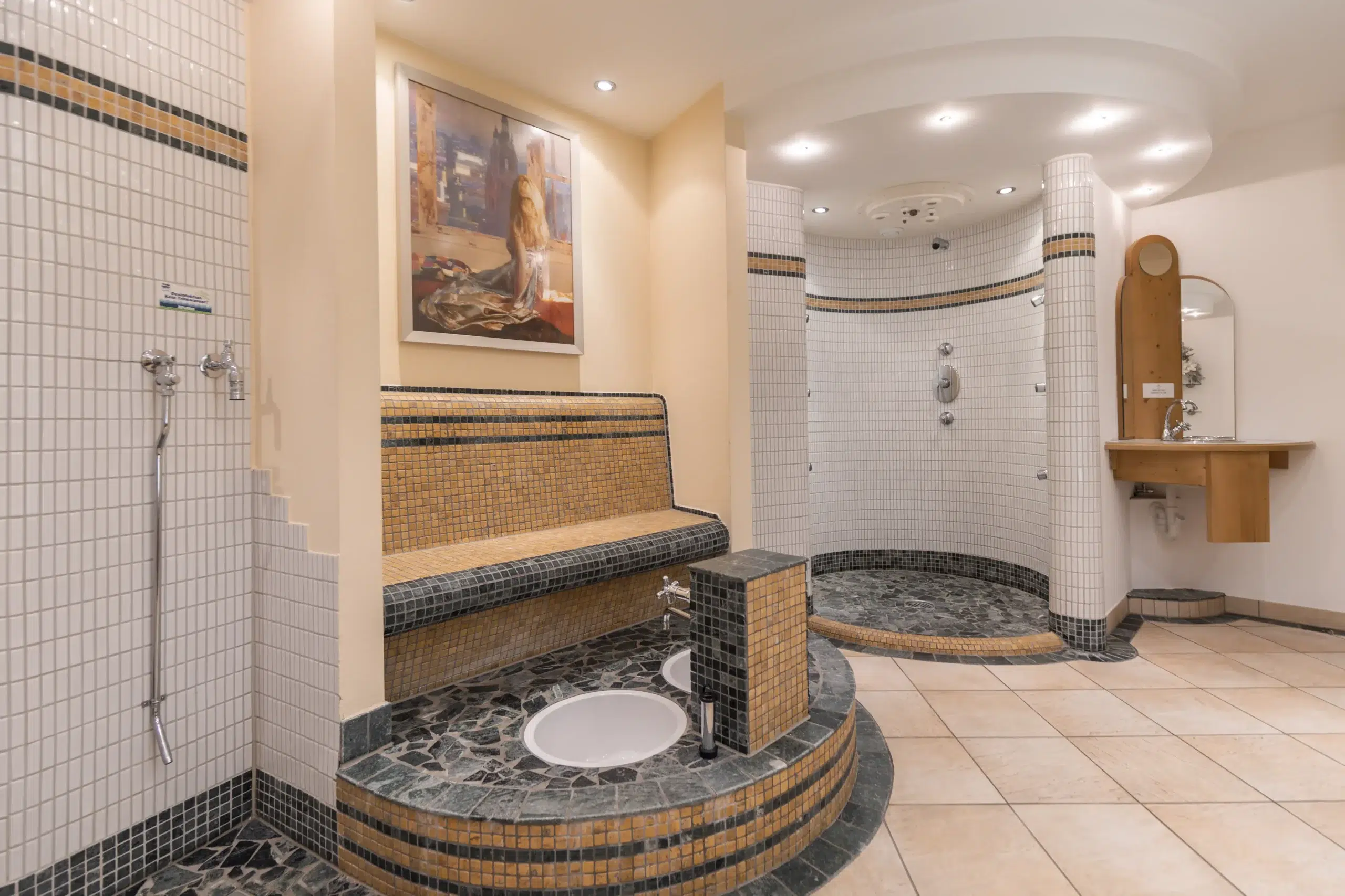 Moderner Spa-Raum in einem Wellnesshotel mit gefliester Sitzbank, Fußbad, offenen Duschen und Schminkbereich.