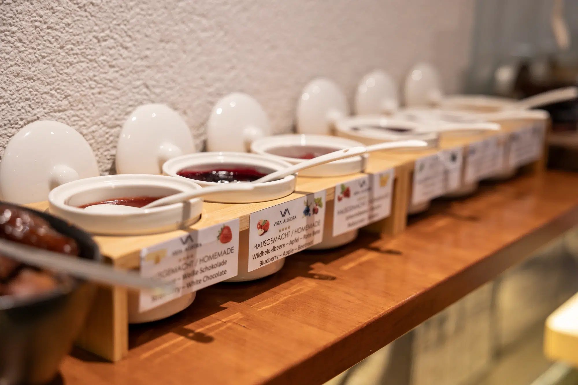 Row of ceramic jars with assorted homemade jams displayed on a restaurant shelf.