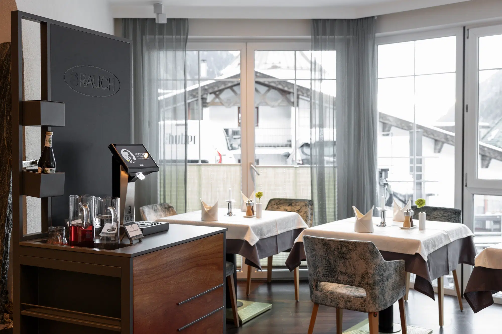 Modern restaurant with set tables, large windows, and a stylish beverage station in the foreground.